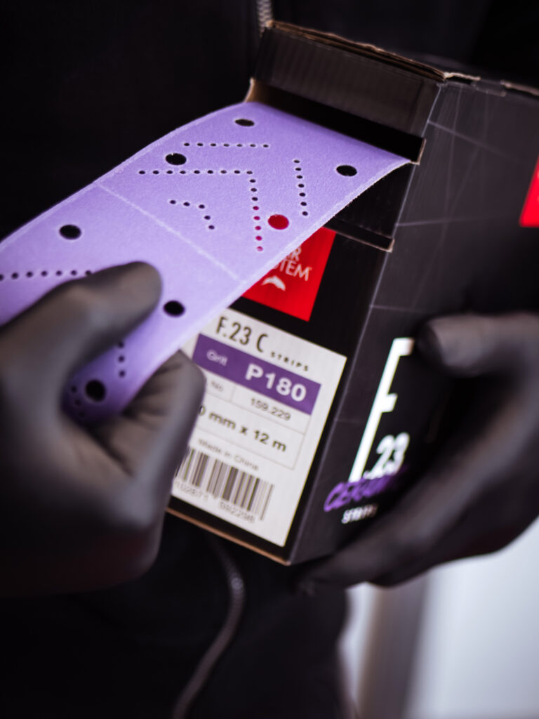 Man grabbing a CARSYSTEM F.23 sanding strip from its box.