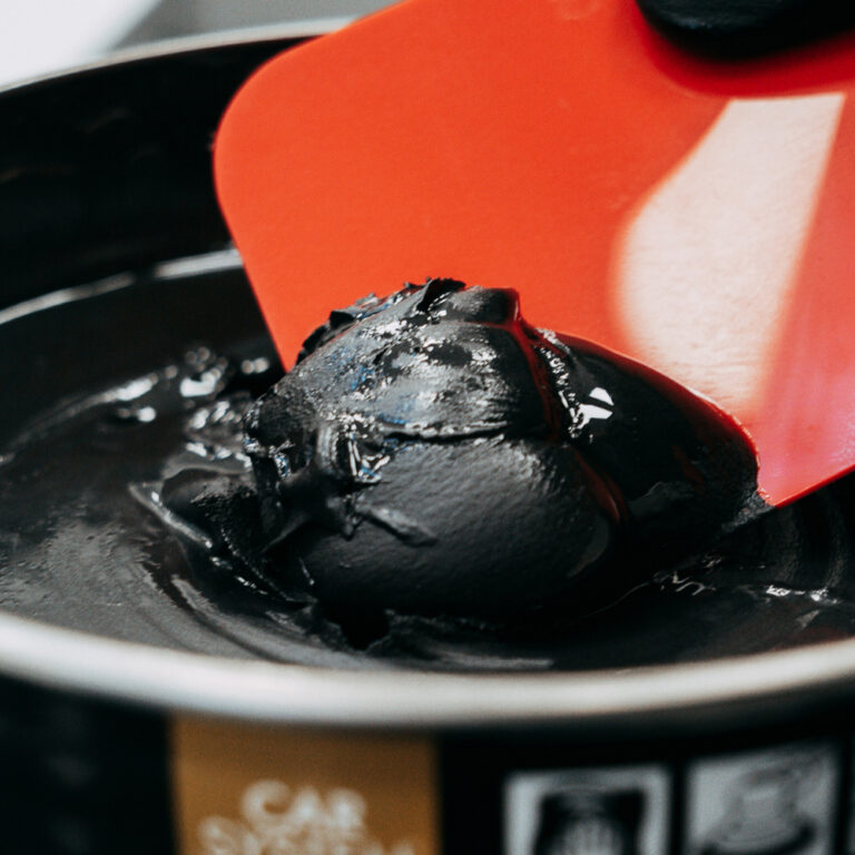 Red putty spatula in a CARSYSTEM Multi Black Rapid multipurpose black putty can.