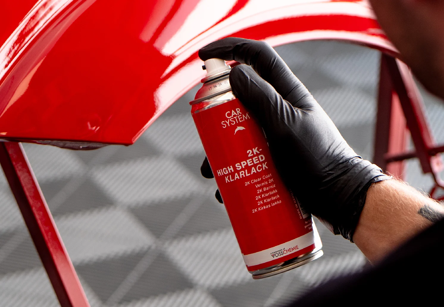 Hand spraying a red car side panel with a can of CARSYSTEM clear coat spray.
